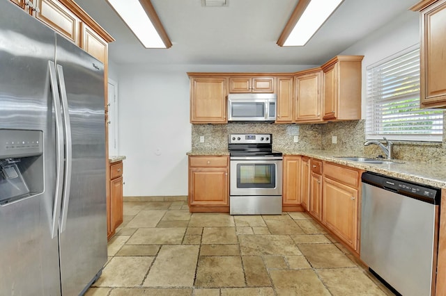 kitchen with light stone countertops, appliances with stainless steel finishes, backsplash, and sink