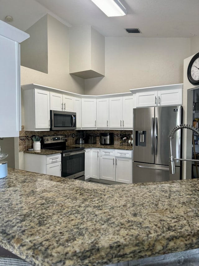 kitchen featuring a high ceiling, white cabinets, decorative backsplash, dark stone countertops, and stainless steel appliances