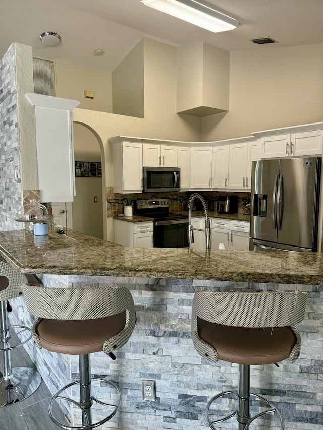 kitchen featuring kitchen peninsula, stainless steel appliances, a high ceiling, white cabinetry, and a breakfast bar area