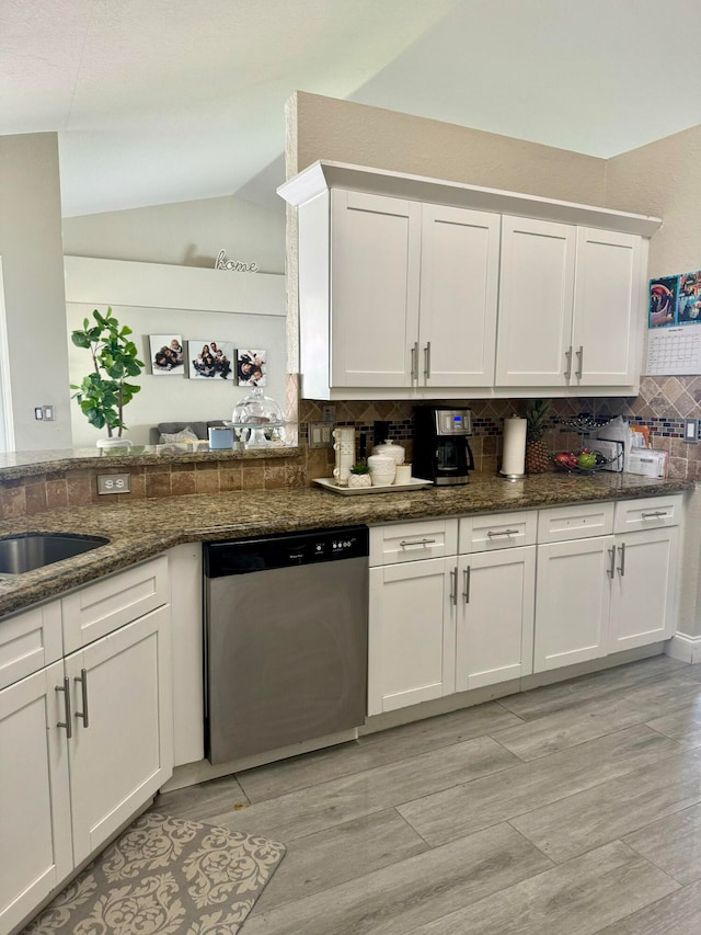 kitchen with dishwasher, dark stone counters, vaulted ceiling, tasteful backsplash, and white cabinetry