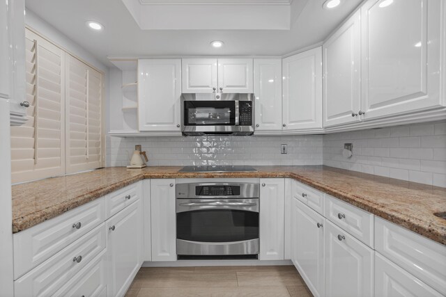 kitchen with white cabinets, light stone countertops, stainless steel appliances, and backsplash