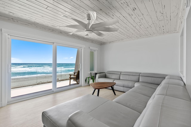 living room featuring a beach view, light hardwood / wood-style floors, ceiling fan, wooden ceiling, and a water view