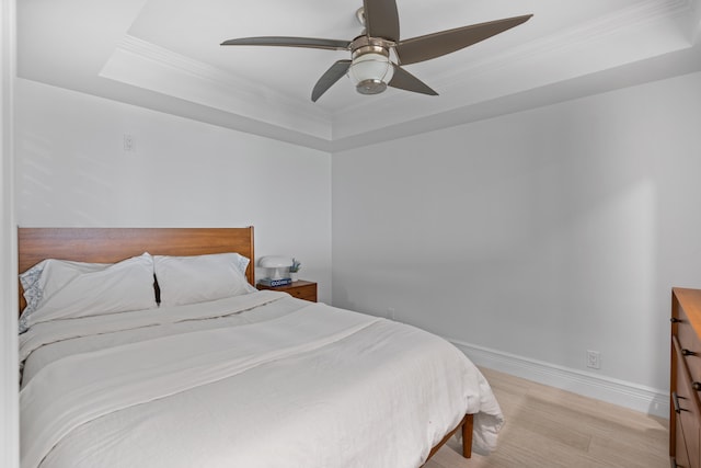 bedroom featuring light hardwood / wood-style flooring, a tray ceiling, crown molding, and ceiling fan