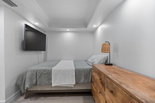 bedroom with ornamental molding, hardwood / wood-style floors, and a tray ceiling