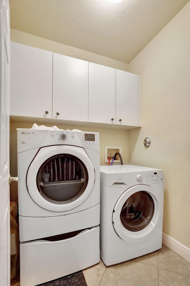 clothes washing area with light tile patterned floors, a textured ceiling, cabinets, and washing machine and clothes dryer