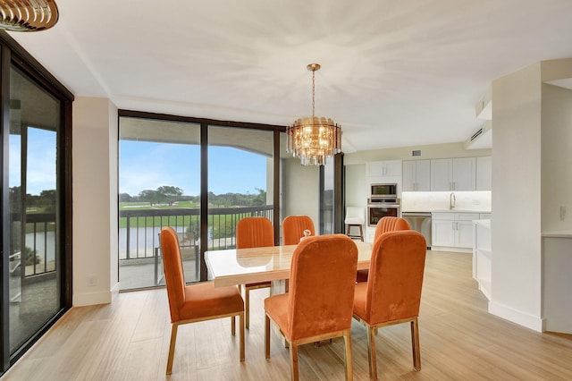 dining room featuring a wall of windows, a water view, light hardwood / wood-style flooring, and an inviting chandelier