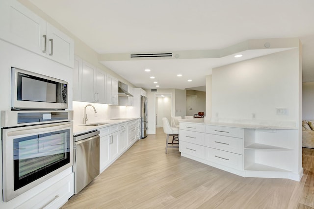 kitchen featuring appliances with stainless steel finishes, white cabinets, sink, and light hardwood / wood-style floors