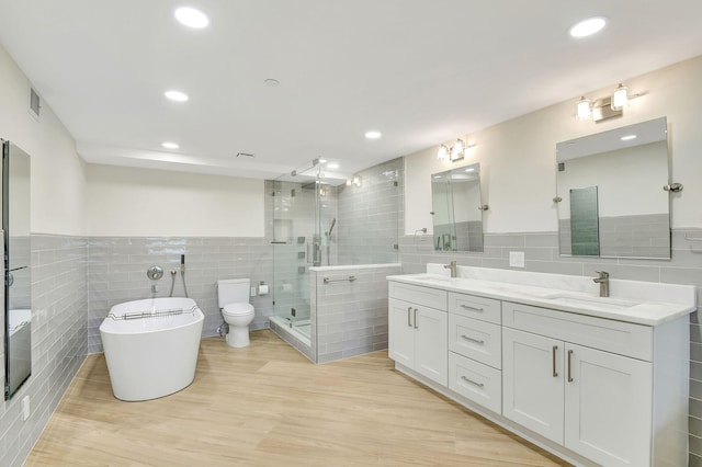 full bathroom with shower with separate bathtub, toilet, tile walls, vanity, and hardwood / wood-style flooring