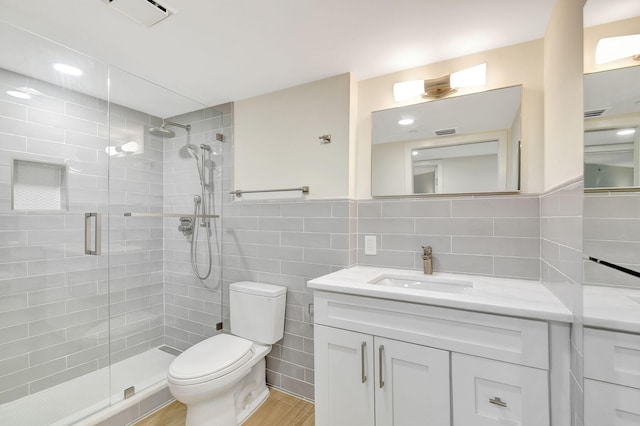 bathroom featuring wood-type flooring, a shower with shower door, toilet, tile walls, and vanity