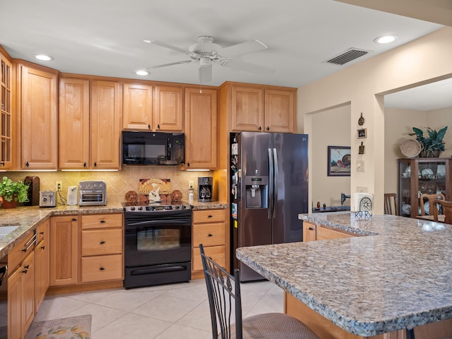 kitchen featuring light tile patterned flooring, ceiling fan, black appliances, and a breakfast bar area