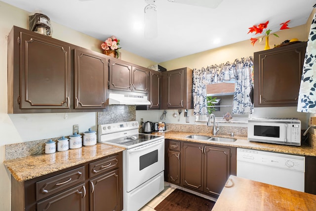 kitchen featuring sink, light tile patterned flooring, dark brown cabinetry, light stone counters, and white appliances