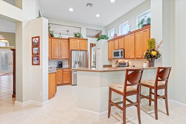 kitchen with appliances with stainless steel finishes, a kitchen bar, kitchen peninsula, decorative backsplash, and light tile patterned floors