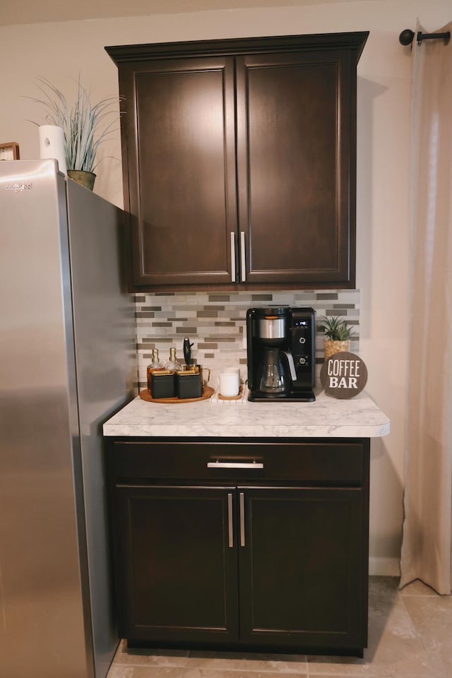 bar with stainless steel fridge, decorative backsplash, and dark brown cabinets