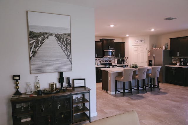 kitchen featuring a kitchen bar, backsplash, a center island, stainless steel appliances, and light tile patterned floors