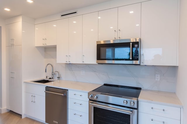 kitchen with white cabinets, sink, light hardwood / wood-style flooring, light stone countertops, and stainless steel appliances