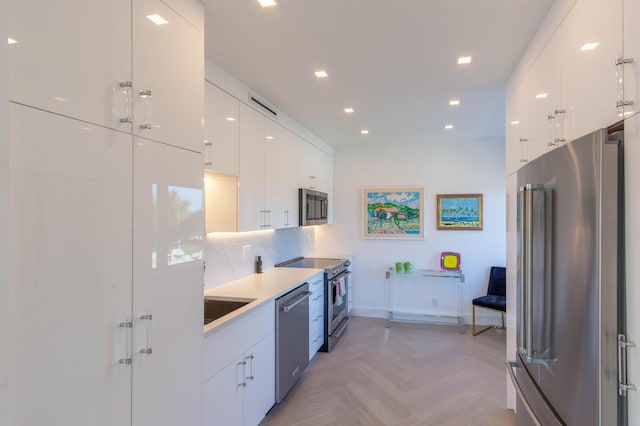 kitchen featuring stainless steel appliances, sink, white cabinetry, tasteful backsplash, and light parquet flooring