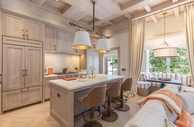 kitchen featuring an island with sink, light brown cabinets, beamed ceiling, pendant lighting, and light parquet flooring