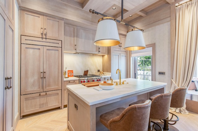 kitchen featuring light brown cabinetry, beamed ceiling, decorative light fixtures, and a center island with sink