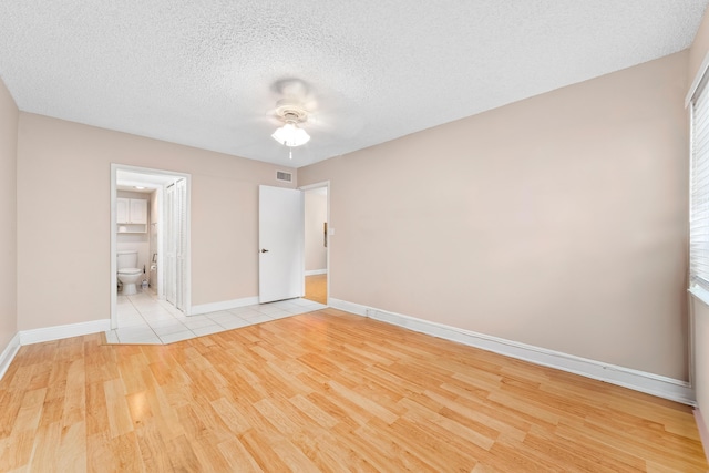 unfurnished bedroom featuring ceiling fan, a textured ceiling, light hardwood / wood-style floors, and ensuite bath