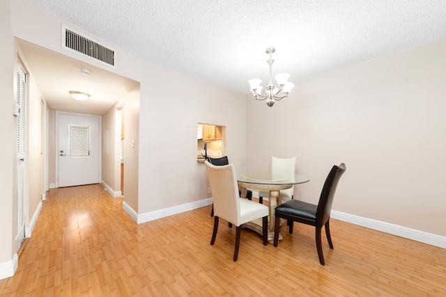 dining area with an inviting chandelier, a textured ceiling, and light wood-type flooring