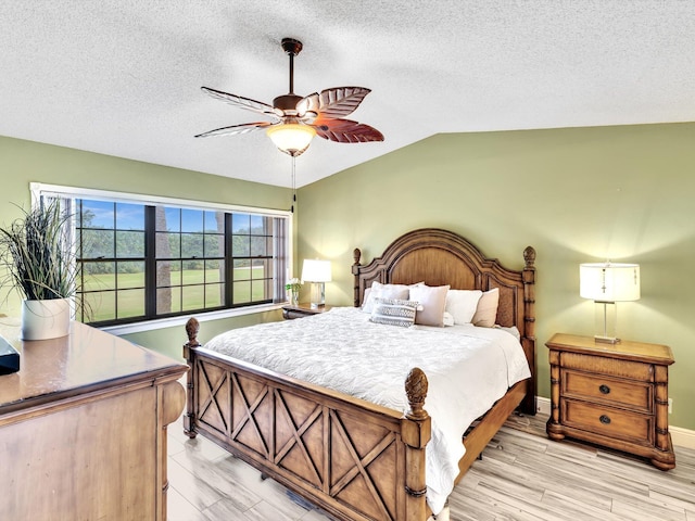 bedroom featuring ceiling fan, a textured ceiling, lofted ceiling, and light wood-type flooring