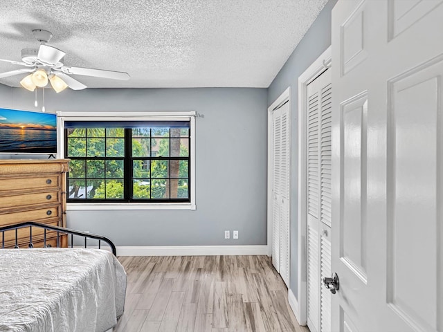 bedroom with light hardwood / wood-style flooring, a textured ceiling, two closets, and ceiling fan