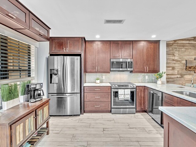 kitchen featuring decorative backsplash, light hardwood / wood-style flooring, stainless steel appliances, sink, and wood walls