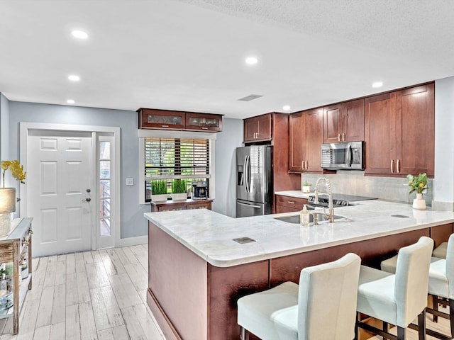 kitchen featuring light hardwood / wood-style floors, kitchen peninsula, stainless steel appliances, and a kitchen bar