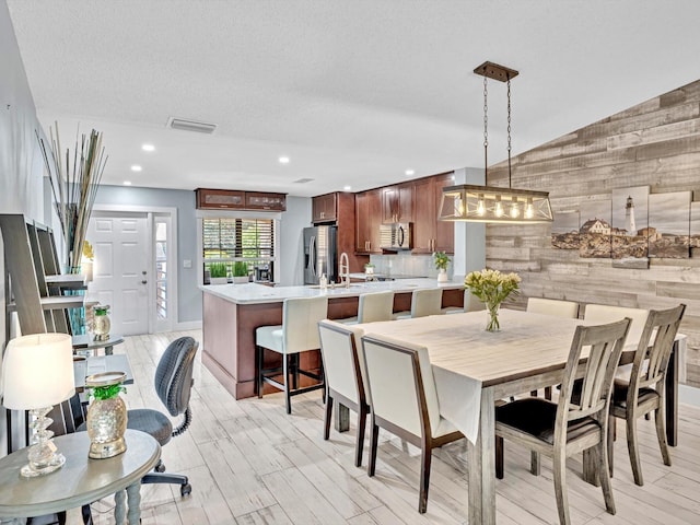 dining room featuring lofted ceiling, wooden walls, sink, a textured ceiling, and light hardwood / wood-style floors