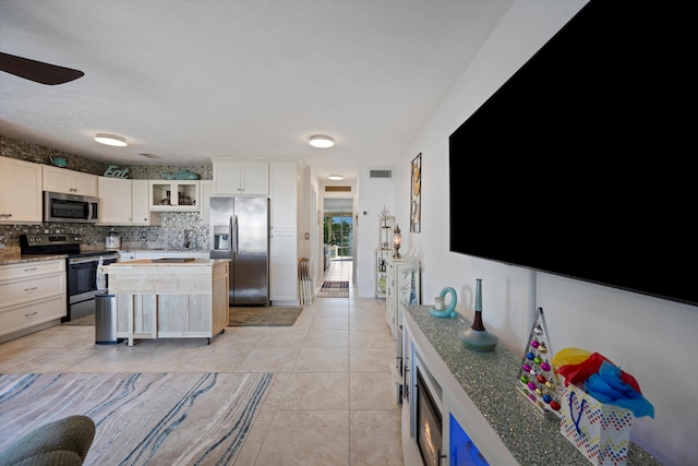 kitchen featuring tasteful backsplash, light stone countertops, light tile patterned flooring, stainless steel appliances, and white cabinets