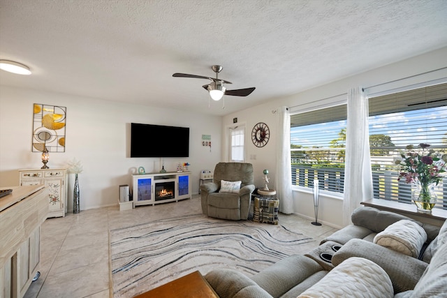 living room featuring a textured ceiling, a fireplace, light tile patterned floors, and ceiling fan