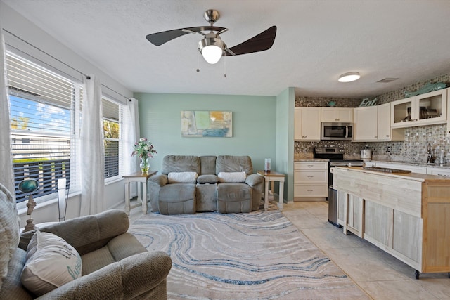 interior space with appliances with stainless steel finishes, a textured ceiling, ceiling fan, decorative backsplash, and light tile patterned floors