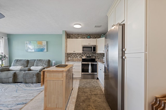 kitchen featuring appliances with stainless steel finishes, a kitchen island, butcher block countertops, backsplash, and white cabinetry