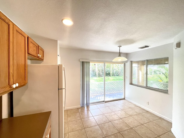 interior space featuring hanging light fixtures, light tile patterned floors, a textured ceiling, and white fridge