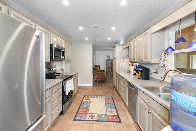 kitchen featuring light tile patterned flooring, stainless steel appliances, a textured ceiling, hanging light fixtures, and cream cabinetry