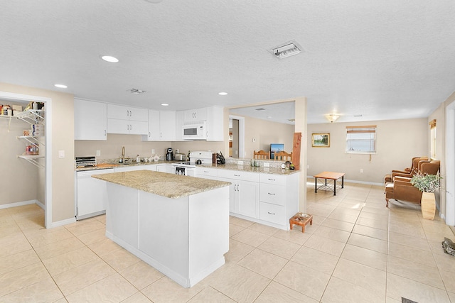 kitchen featuring light tile patterned flooring, a kitchen island, white cabinetry, kitchen peninsula, and white appliances