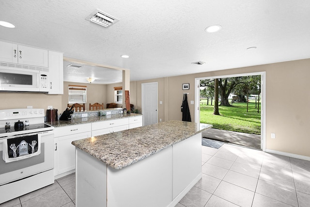 kitchen featuring a textured ceiling, light tile patterned floors, a kitchen island, white cabinetry, and white appliances