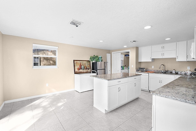 kitchen featuring white cabinetry, a kitchen island, stainless steel refrigerator, and light stone countertops