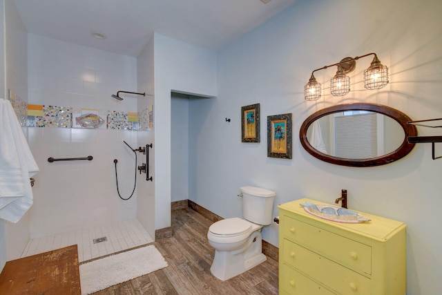 bathroom with toilet, vanity, wood-type flooring, and tiled shower