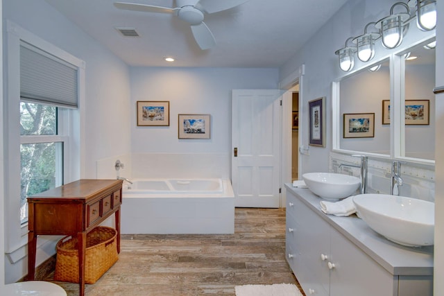 bathroom with wood-type flooring, vanity, tiled bath, and ceiling fan