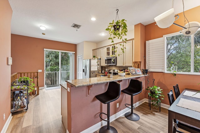 kitchen with light stone countertops, appliances with stainless steel finishes, cream cabinets, light hardwood / wood-style floors, and pendant lighting