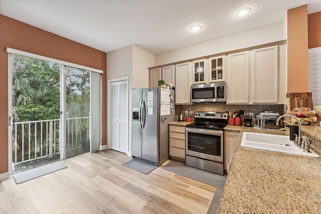 kitchen with light wood-type flooring, sink, stainless steel appliances, and a textured ceiling