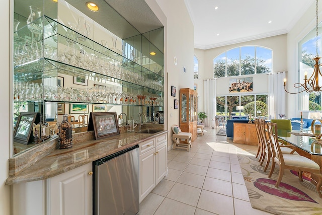 bar with sink, crown molding, light tile patterned floors, white cabinets, and light stone counters