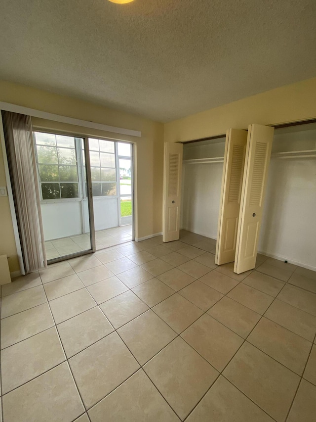 unfurnished bedroom with access to exterior, a textured ceiling, multiple closets, and light tile patterned flooring