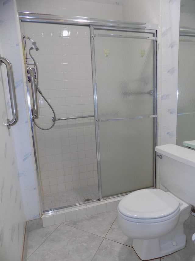 bathroom with a shower with door, toilet, and tile patterned flooring