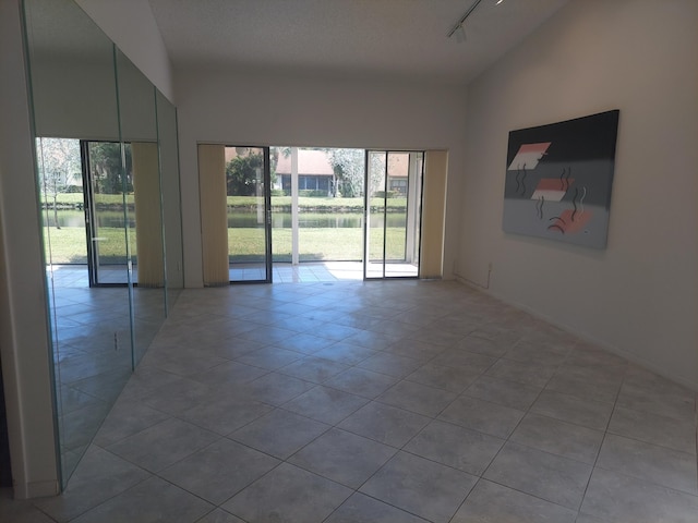 tiled empty room with lofted ceiling, a textured ceiling, and rail lighting