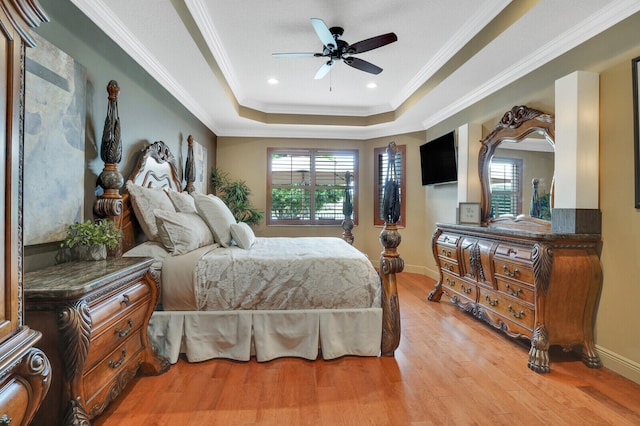 bedroom featuring a tray ceiling, multiple windows, ceiling fan, and light wood-type flooring