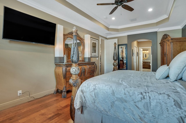 bedroom with hardwood / wood-style floors, connected bathroom, a tray ceiling, and ceiling fan