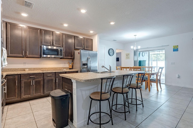 kitchen with a breakfast bar, sink, decorative light fixtures, appliances with stainless steel finishes, and an island with sink