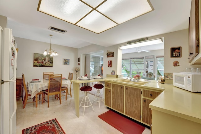 kitchen featuring a breakfast bar area, hanging light fixtures, kitchen peninsula, sink, and white appliances